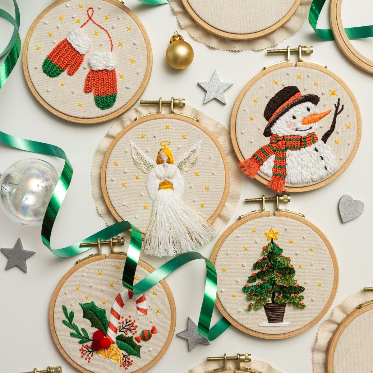 May include: Eight embroidered Christmas ornaments with wooden hoops. The ornaments feature a snowman, an angel, a Christmas tree, candy canes, and mittens. The ornaments are on a white background with green ribbon and gold stars.