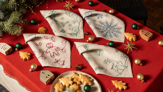 Embroidered Christmas linen napkins on a red tablecloth with Christmas ornaments.