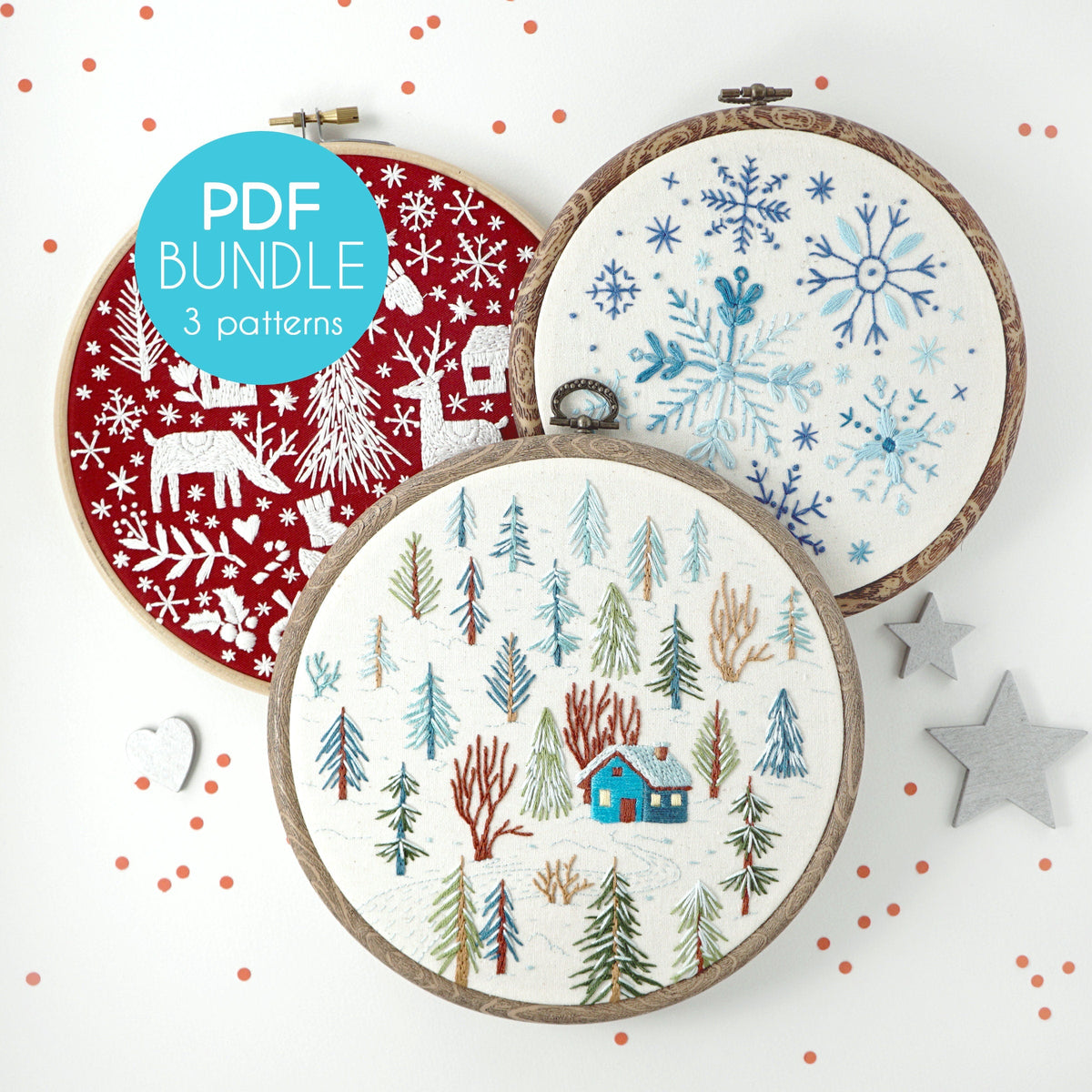 May include: Three embroidery hoop patterns for winter holidays. The first hoop features a red background with white snowflakes, deer, and trees. The second hoop features a white background with a blue cabin and green trees. The third hoop features a