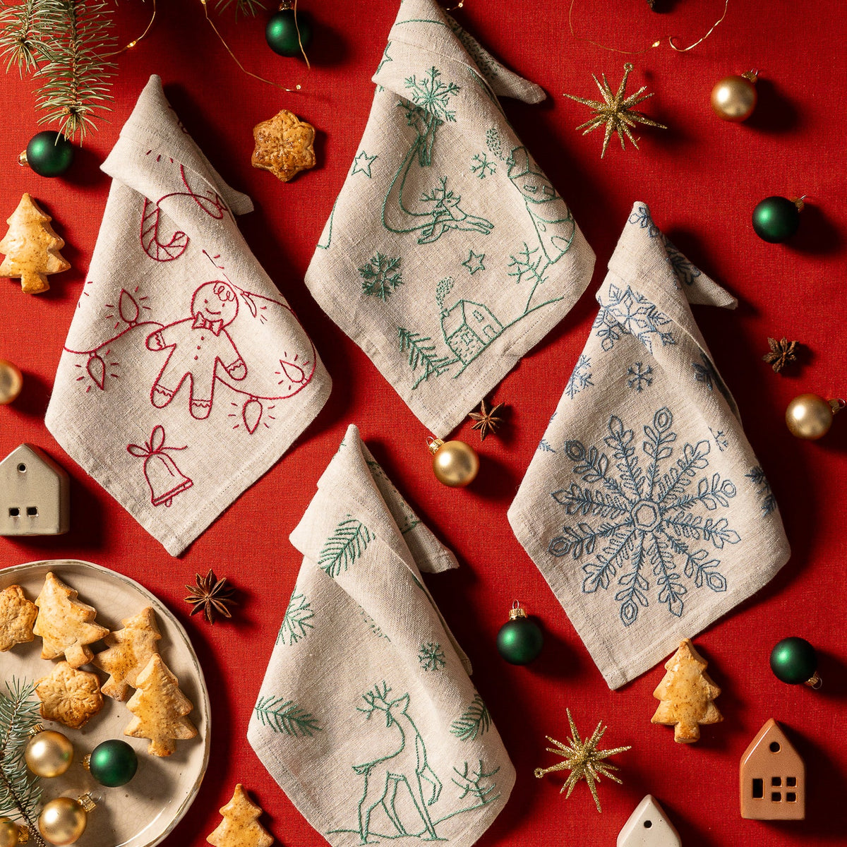 May include: Embroidered hoop art with a winter scene. The design features a small cabin, a blue and white ombre Christmas tree, and the text "Merry and Bright" in cursive script. The background is white with scattered snowflakes.