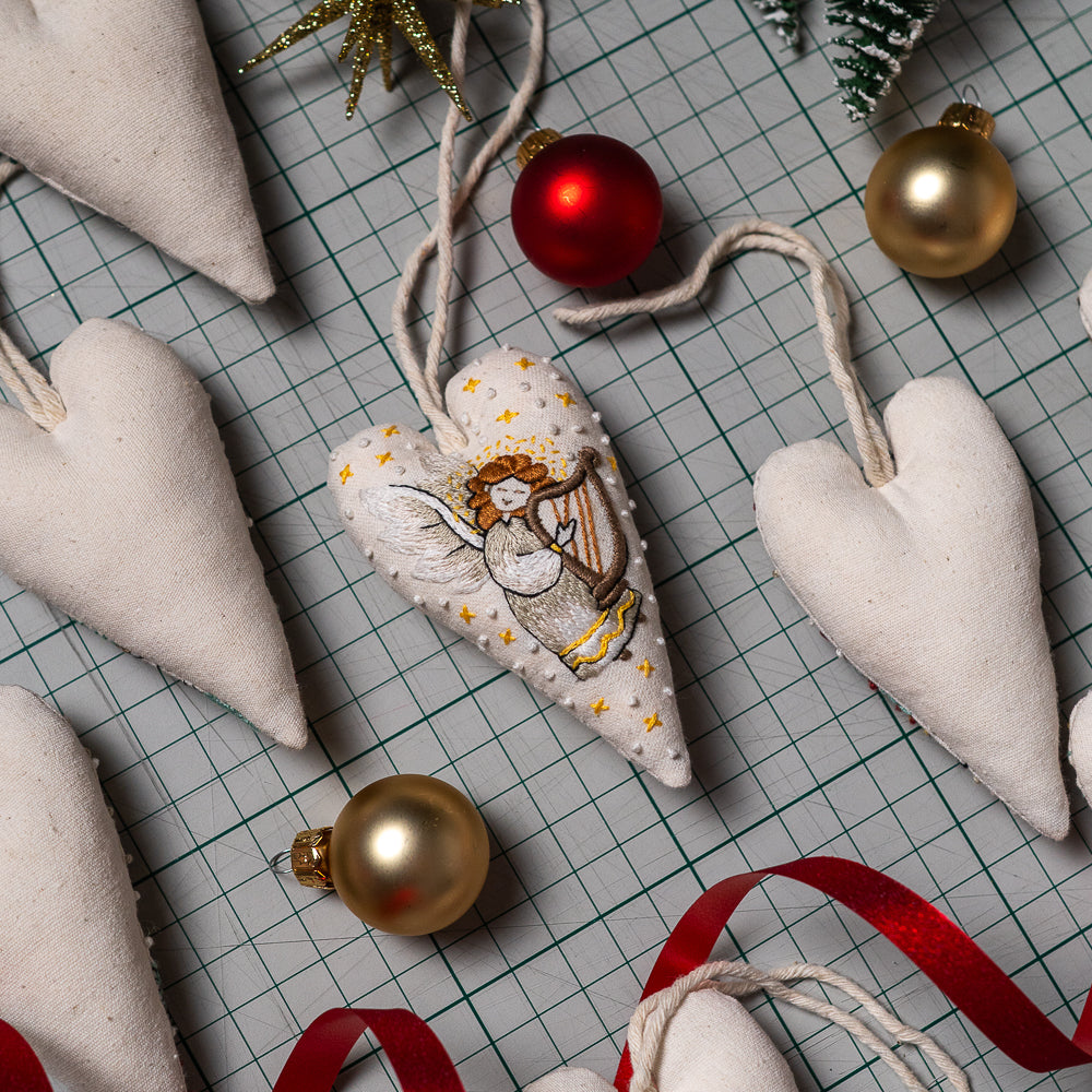 A heart-shaped Christmas ornament with embroidered angel details and gold stars by Why Knot Stitches
