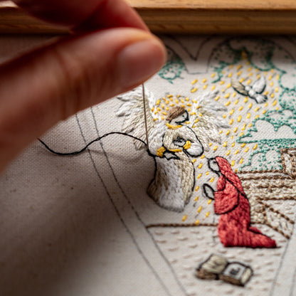 Close-up of hand embroidery in progress showing Angel Gabriel, Mary in a red robe, a dove and detailed stitching.