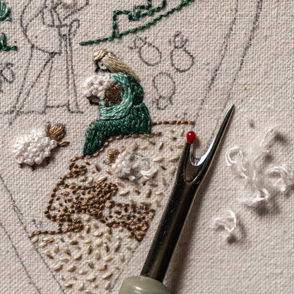 Detailed hand embroidery of a shepherd and textured sheep made with Colonial Knots, with embroidery scissors beside the Christian Nativity design.