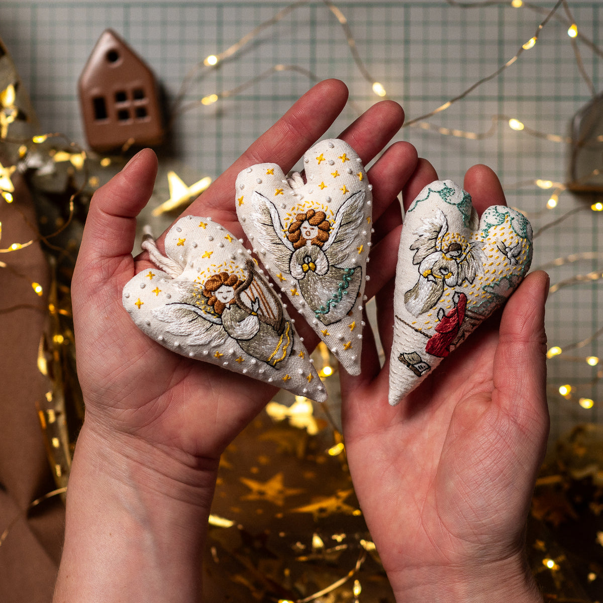 Three handmade embroidered Christmas heart ornaments featuring a harp-playing angel, a herald angel and the Annunciation scene.