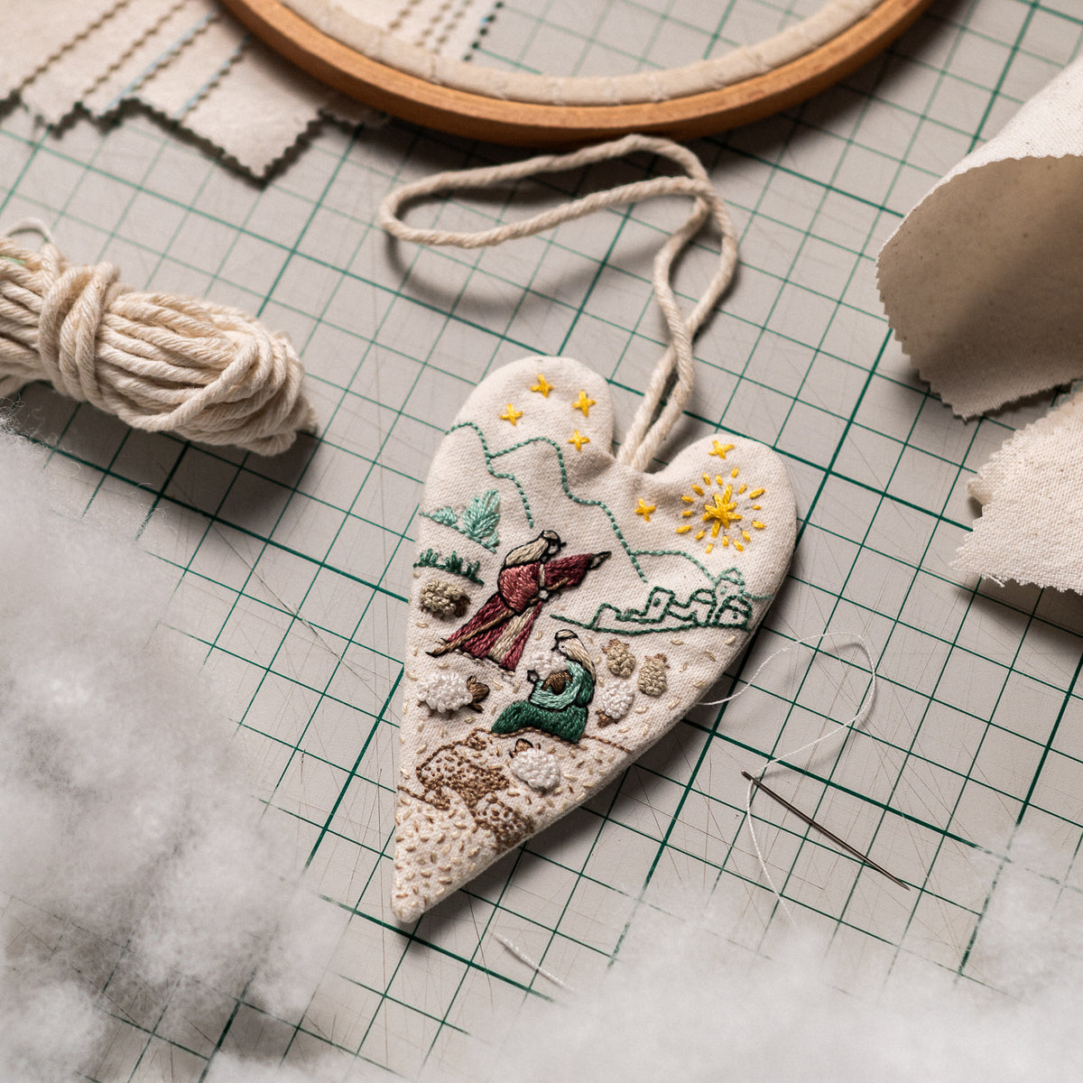 The Shepherds of Bethlehem embroidered heart ornament on a cutting mat with cotton hanging cord and polyester fiberfill for DIY Christmas ornament making.