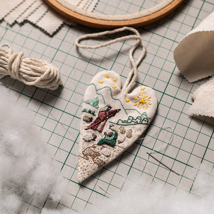 The Shepherds of Bethlehem embroidered heart ornament on a cutting mat with cotton hanging cord and polyester fiberfill for DIY Christmas ornament making.