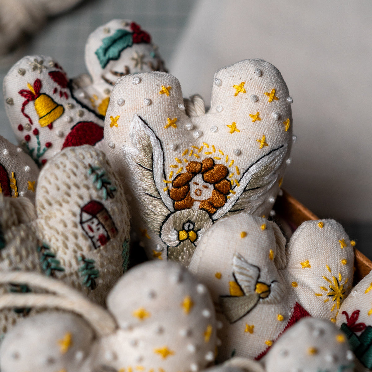 Embroidered herald angel heart ornament nestled among other handmade Christmas heart ornaments with festive designs.