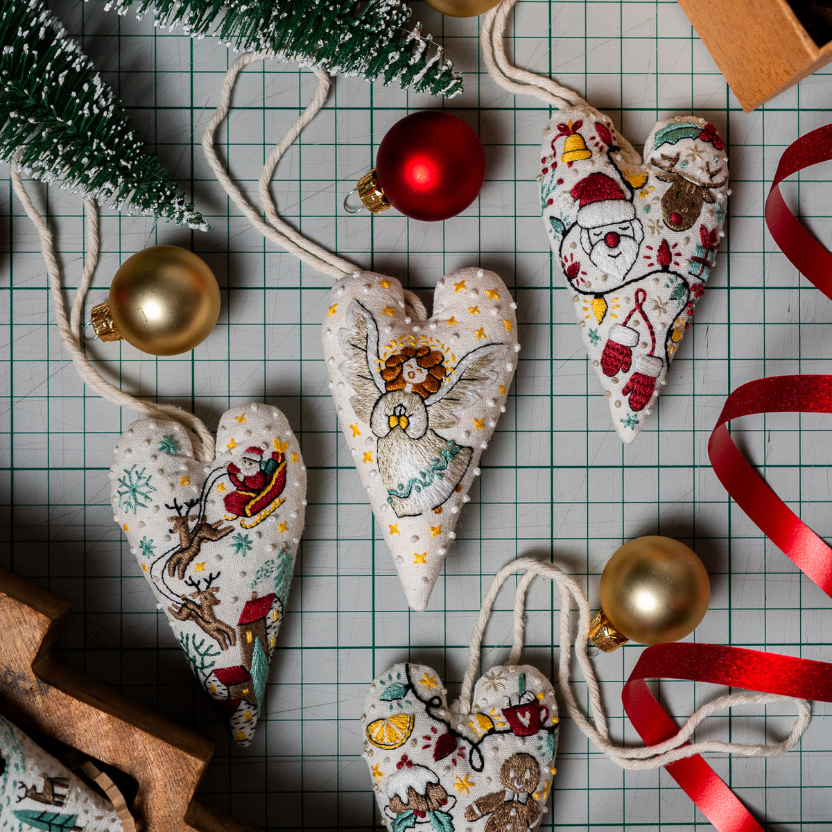 Overhead view of a herald angel embroidered heart ornament alongside Santa and other Christmas ornament designs, ribbons and baubles.