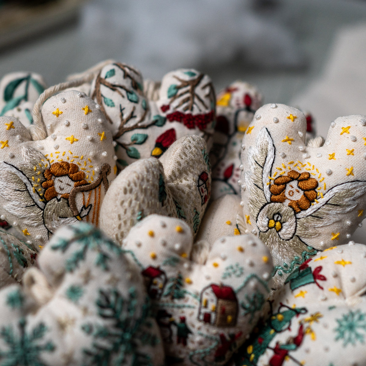 Two embroidered angel heart ornaments with golden hair and silver wings displayed among a collection of Christmas embroidery designs.