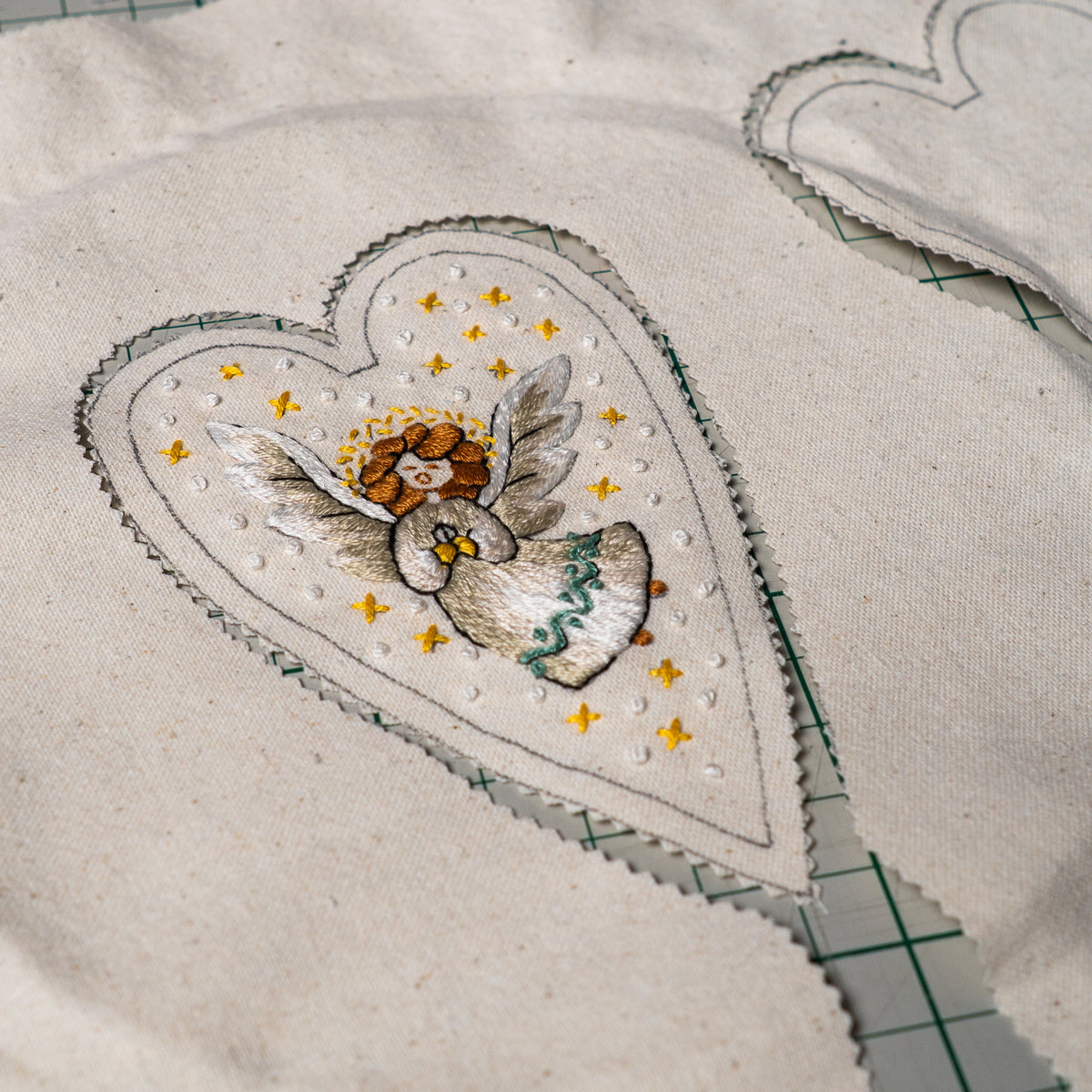 Embroidered herald angel design on heart-shaped linen fabric, cut with pinking shears and ready to sew into a Christmas ornament.