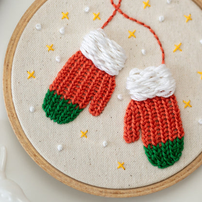 May include: Embroidered hoop art featuring two red and green mittens with white cuffs. The mittens are stitched on a white canvas background with yellow and white dots.