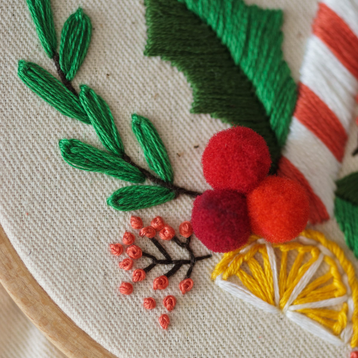 May include: Embroidered Christmas wreath with red and white candy canes, green holly leaves, red pom-poms, and a yellow lemon slice.