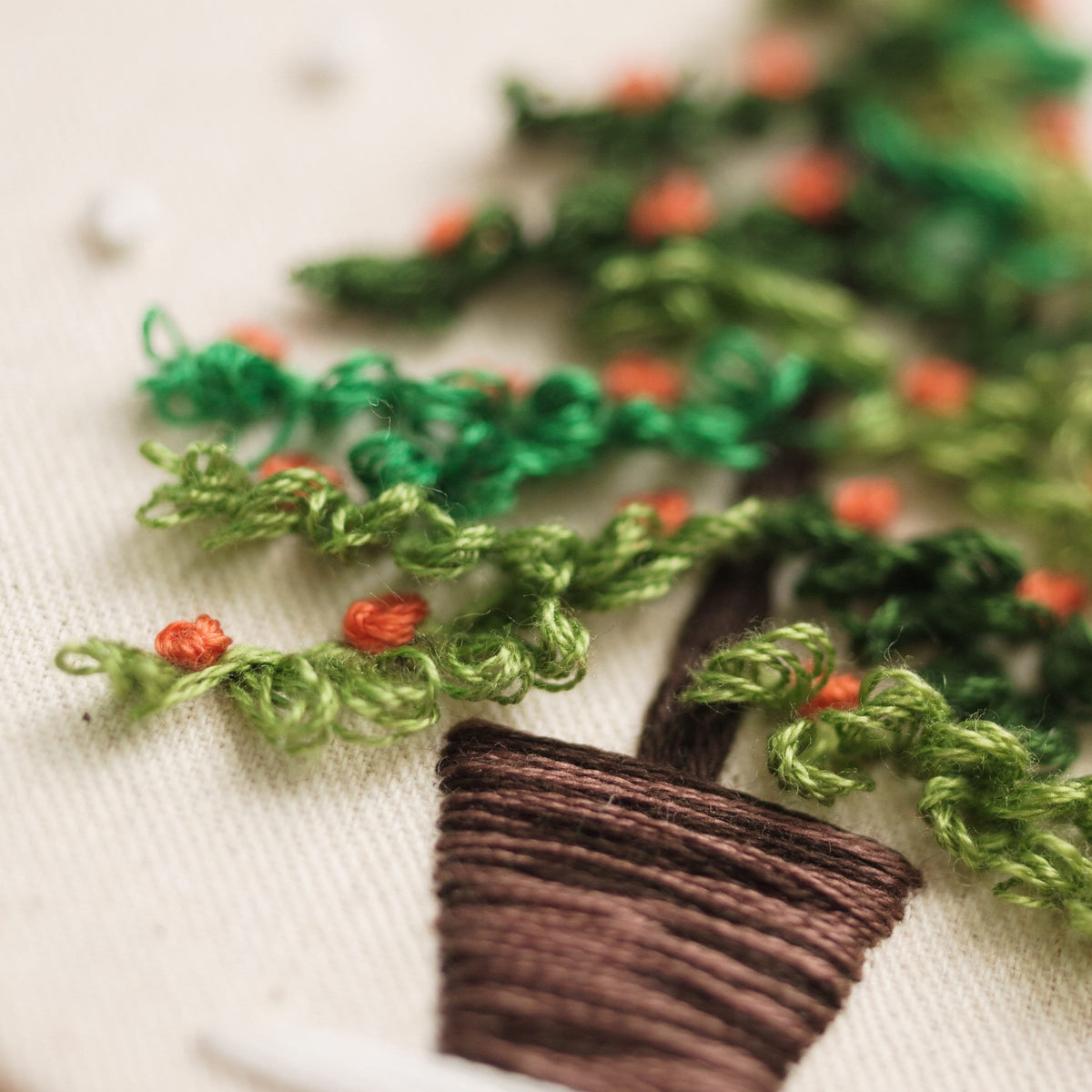 May include: Close-up of a green embroidered tree with red berries in a brown pot. The tree is stitched with a fluffy texture.