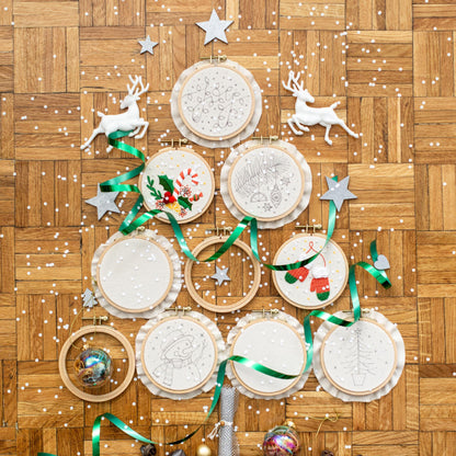 May include: A set of 10 embroidery hoops with various Christmas-themed designs, including a snowman, a Christmas tree, and a stocking. The hoops are arranged in a circle on a wooden surface.