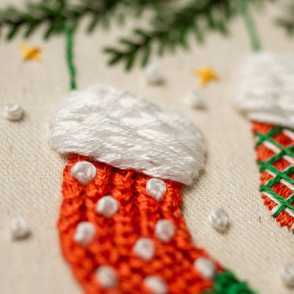 May include: Close-up of a hand-stitched Christmas stocking with a white pom-pom on top and red and white knit details.