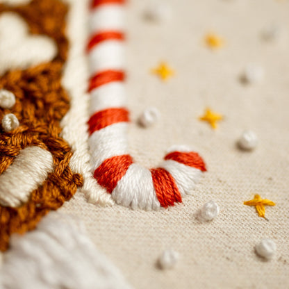 May include: Close-up of a white fabric with red and white candy cane embroidery. The candy cane is stitched in a curved shape. The fabric is decorated with small yellow stars.