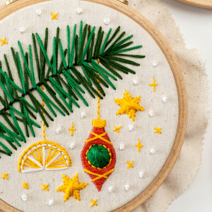 May include: Embroidered hoop art featuring a green palm tree with yellow stars and a red and green Christmas ornament hanging from a branch.
