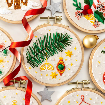 May include: A set of five embroidery hoops with various Christmas-themed designs. The designs include a pine branch with ornaments, a holly sprig with berries, a gingerbread house, and a candy cane. The hoops are all made of wood and have a natural 