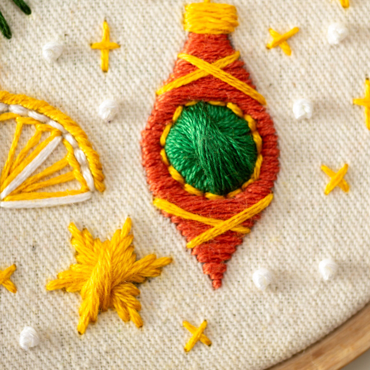 May include: Close-up of a hand-stitched ornament with a green center, orange and yellow stitching, and a white background.