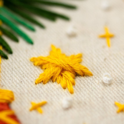 May include: Close-up of a yellow embroidered star on a white fabric background. The star is made of yarn and has a simple, classic design.