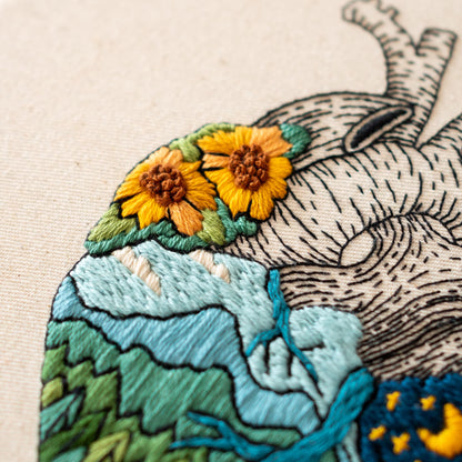 May include: Embroidered heart with a detailed anatomical design, featuring a blue and green landscape with a cluster of yellow and orange sunflowers at the top.