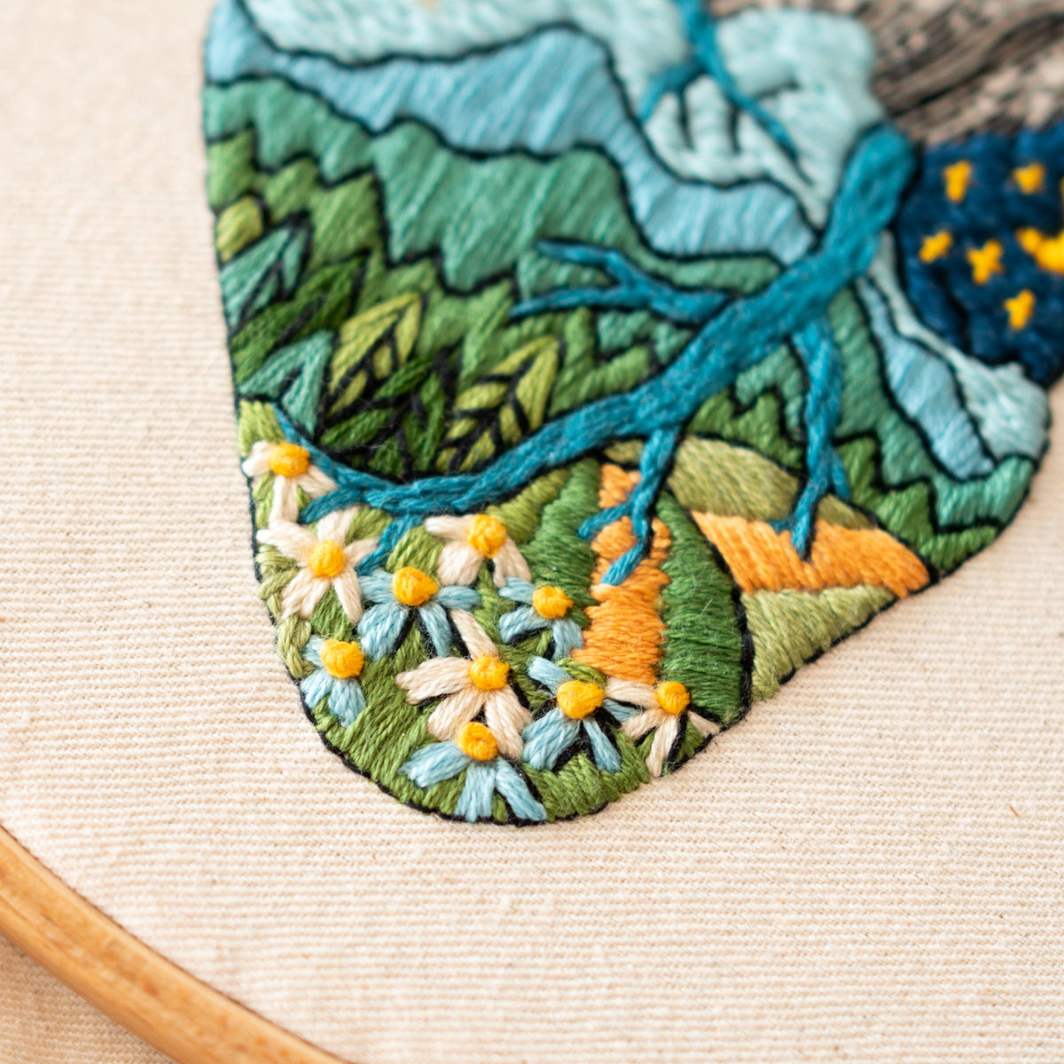May include: Embroidered design of a landscape with mountains, trees, and flowers. The design is stitched in shades of blue, green, yellow, and orange on a white fabric.