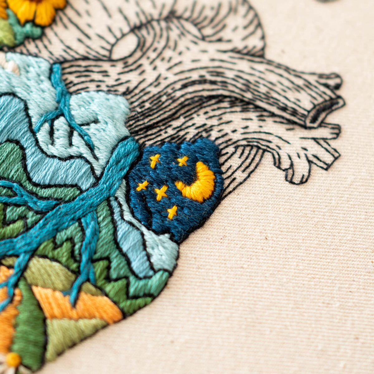 May include: Embroidered heart with a blue and green landscape design. The heart has a small blue patch with a yellow crescent moon and yellow stars.