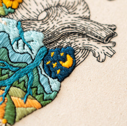 May include: Embroidered heart with a blue and green landscape design. The heart has a small blue patch with a yellow crescent moon and yellow stars.
