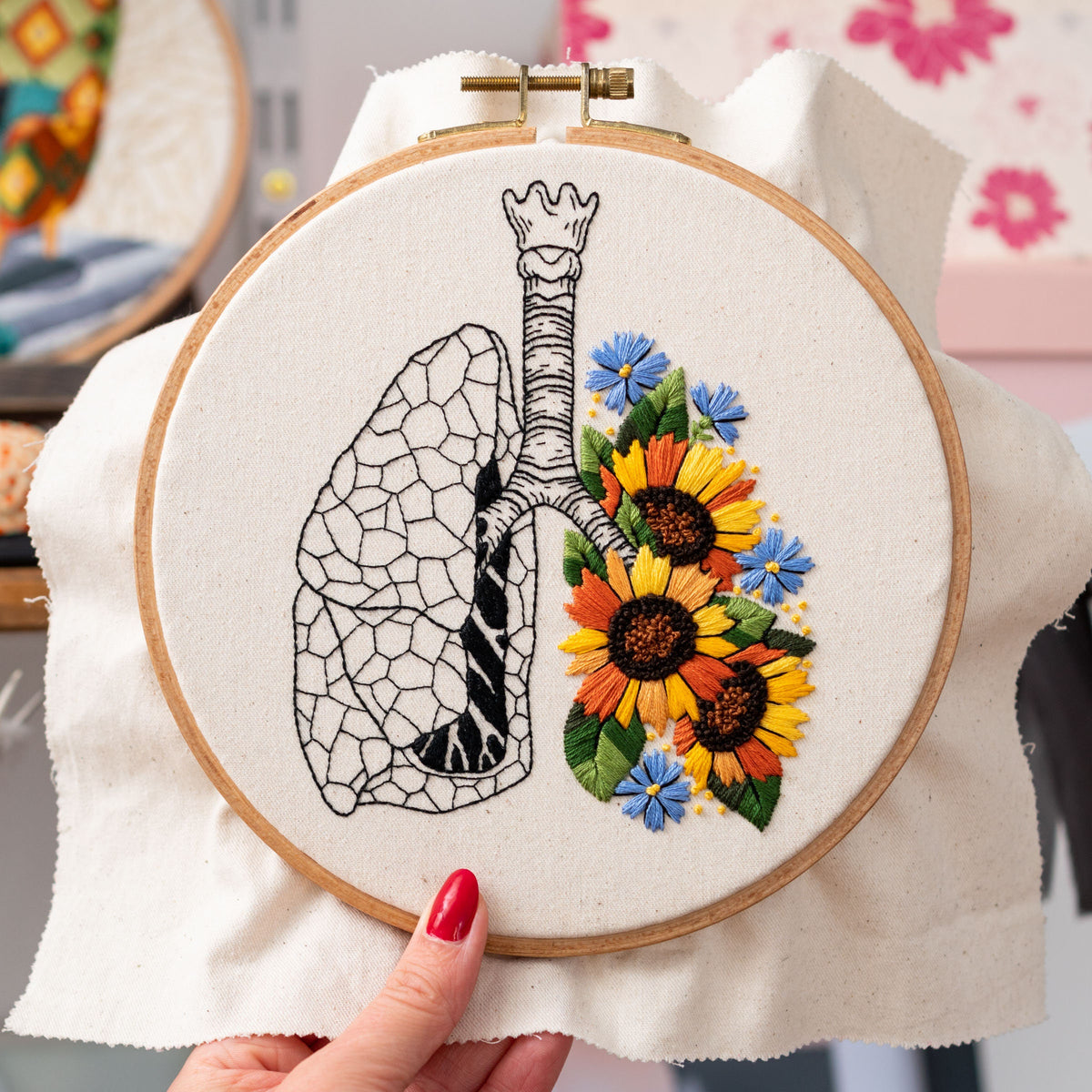 May include: Embroidered hoop art featuring a black and white anatomical illustration of a lung with a cluster of yellow, orange, and blue flowers.