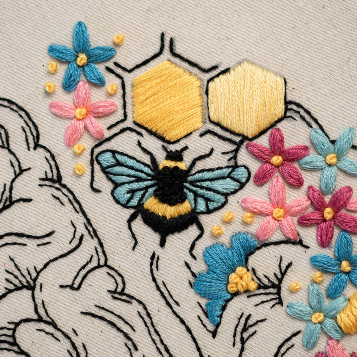 May include: Embroidered design featuring a bee on a honeycomb with surrounding flowers in shades of pink, blue, and yellow. The bee is black and yellow with blue wings. The flowers are embroidered in a variety of styles.