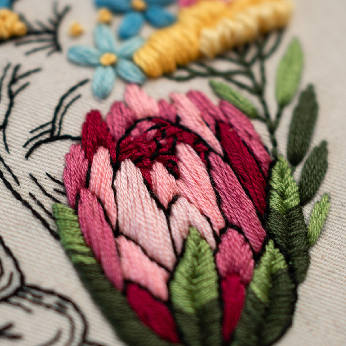May include: Close-up of a pink and red embroidered flower with green leaves. The flower is stitched with a detailed, textured design.