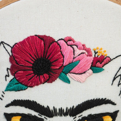May include: Embroidered floral design with a red poppy, pink peonies, and green leaves. The design is on a white canvas and is part of a larger embroidery project.