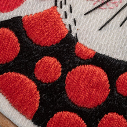 May include: Close-up of a red and black fabric with a polka dot pattern. The fabric is stitched with red thread and has a white background.