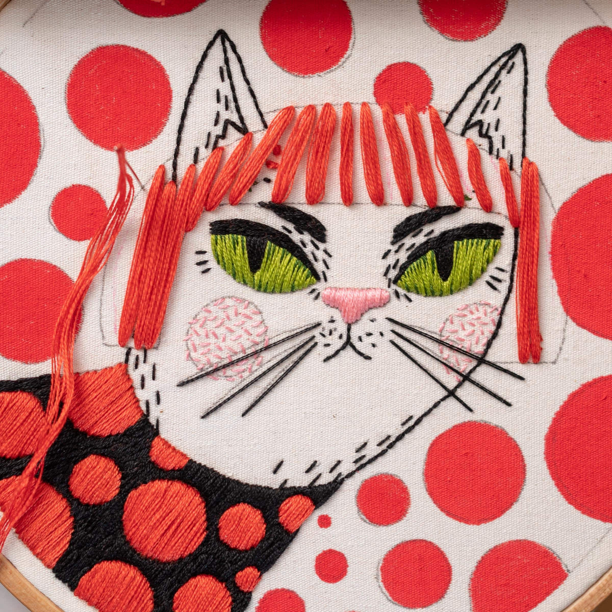 May include: Embroidered white cat with red hair and green eyes on a white background with red polka dots.