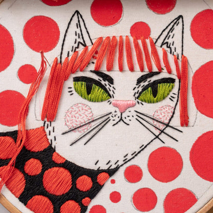 May include: Embroidered white cat with red hair and green eyes on a white background with red polka dots.