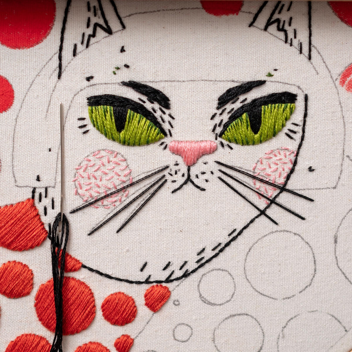 May include: Close-up of a white cat embroidered on a white fabric with green eyes, pink nose, and black whiskers. The cat is surrounded by red and white polka dots.