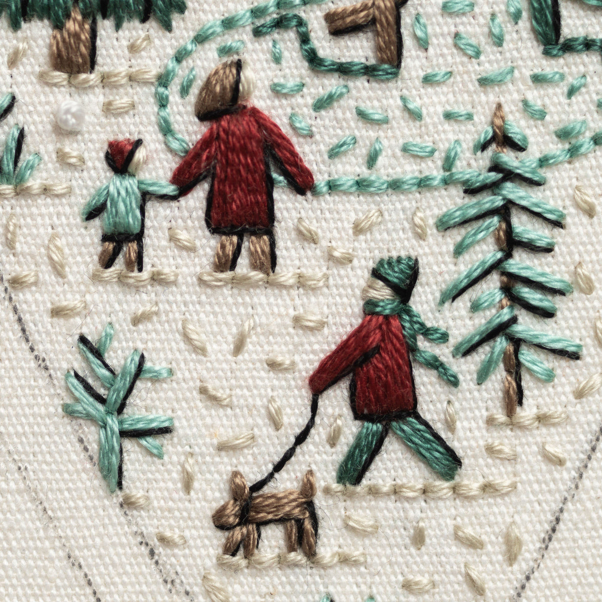 May include: Embroidered image of a winter scene with three people walking in the snow. One person is walking a brown dog on a leash. The scene is stitched in red, green, and brown thread on a white fabric background.