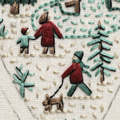 May include: Embroidered image of a winter scene with three people walking in the snow. One person is walking a brown dog on a leash. The scene is stitched in red, green, and brown thread on a white fabric background.