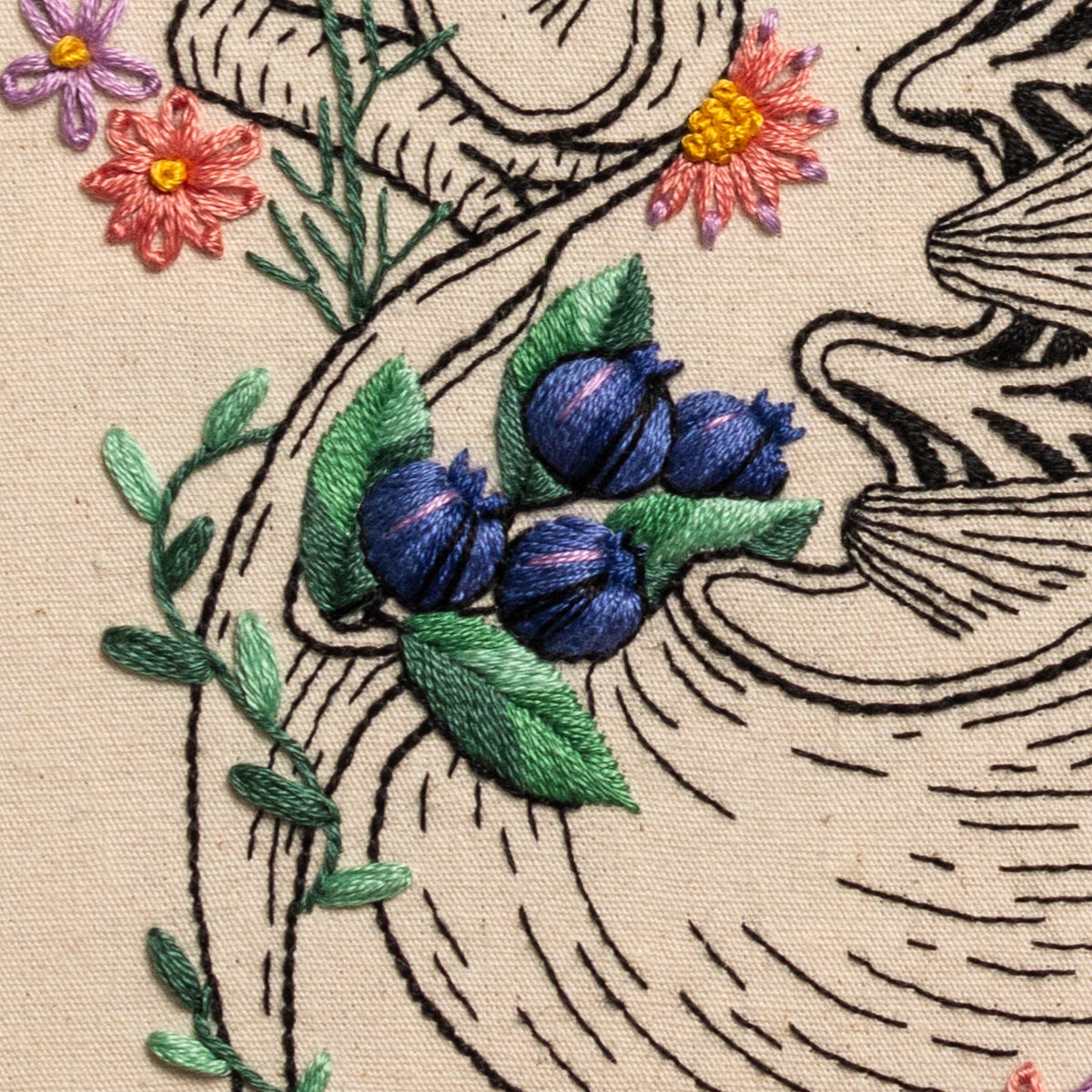 May include: Close-up of an embroidered design featuring a cluster of blueberries with green leaves, surrounded by a black and white line drawing of a seashell.