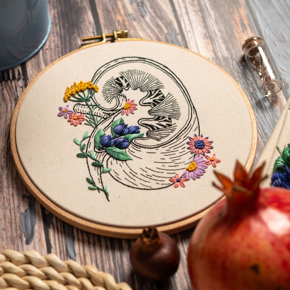 May include: Embroidered hoop art featuring a detailed anatomical illustration of a kidney with delicate floral accents in shades of yellow, pink, blue, and purple.