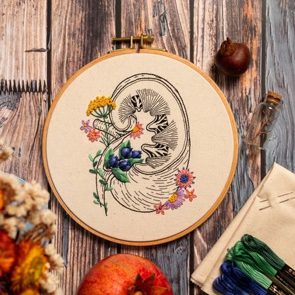 May include: Embroidered hoop art featuring a detailed anatomical illustration of a kidney surrounded by colorful flowers and berries. The hoop is made of wood and has a natural linen fabric.