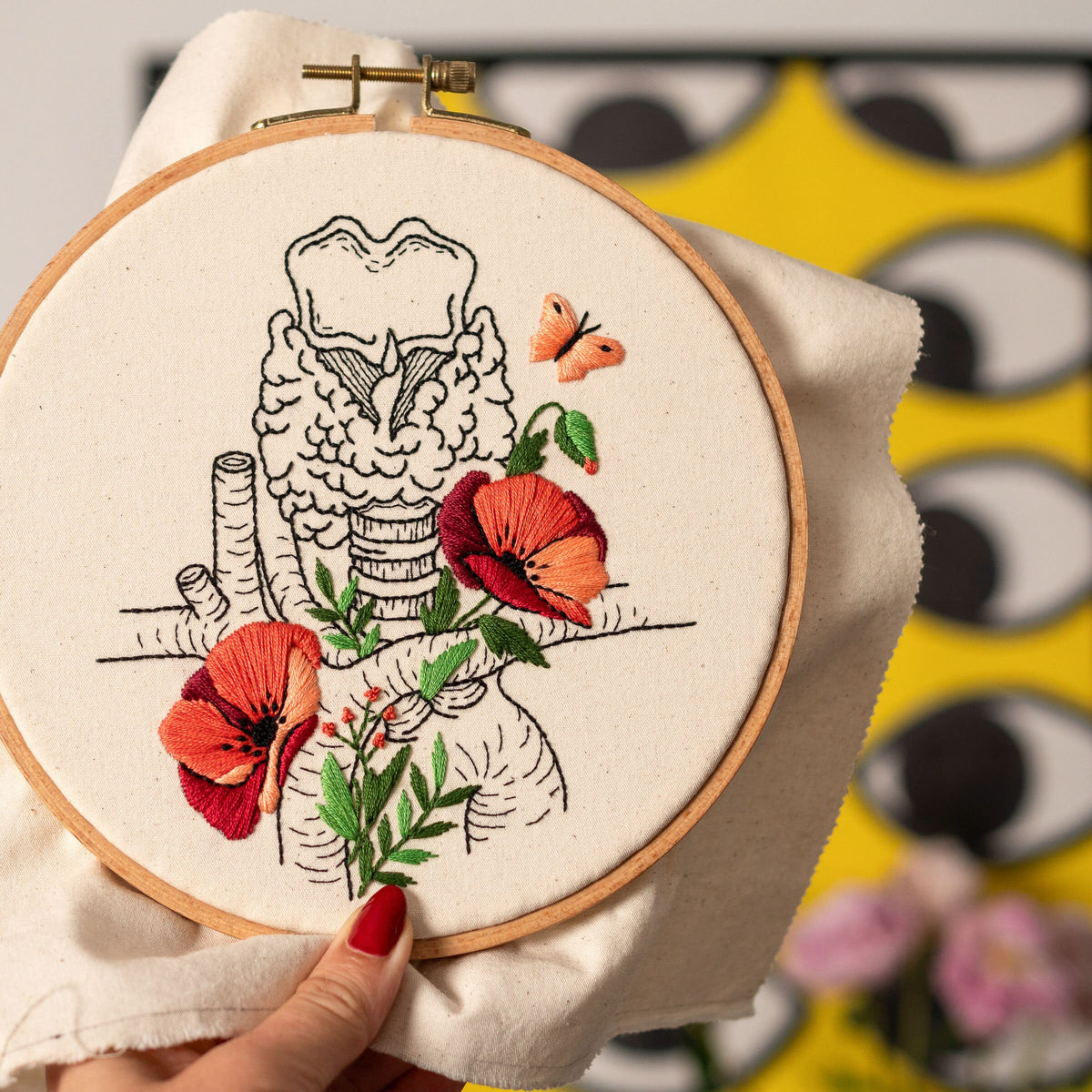 May include: Embroidered hoop art featuring a detailed anatomical illustration of the human trachea with red poppy flowers and a butterfly.