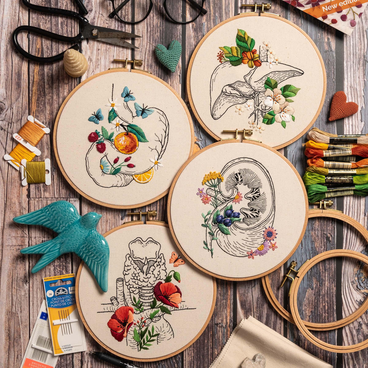 May include: Four embroidery hoops with different anatomical organs embroidered with flowers. The organs are the stomach, liver, kidney, and trachea. The flowers are in various colors, including red, pink, blue, and yellow.