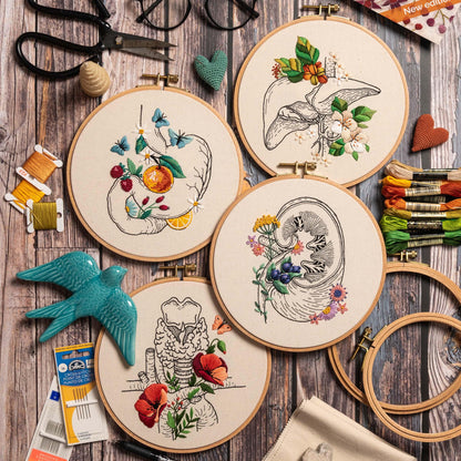 May include: Four embroidery hoops with different anatomical organs embroidered with flowers. The organs are the stomach, liver, kidney, and trachea. The flowers are in various colors, including red, pink, blue, and yellow.