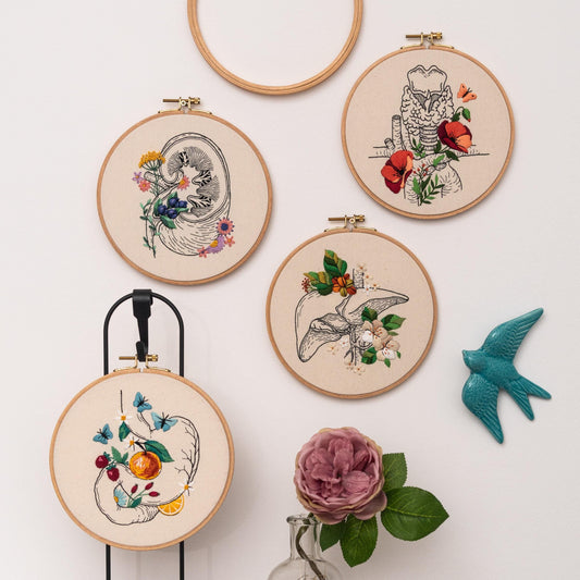 May include: Four embroidery hoops with different anatomical organs embroidered with colorful flowers. The organs include a kidney, a liver, a larynx, and a stomach.