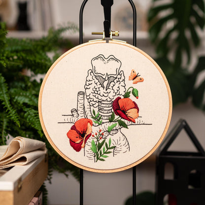 May include: Embroidered hoop art featuring a detailed anatomical illustration of the larynx with red poppy flowers and a butterfly.