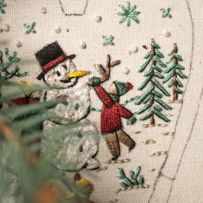 May include: Embroidered design of a snowman with a black top hat and a child throwing a snowball at it. The scene is set in a snowy forest with green trees and white snowflakes.