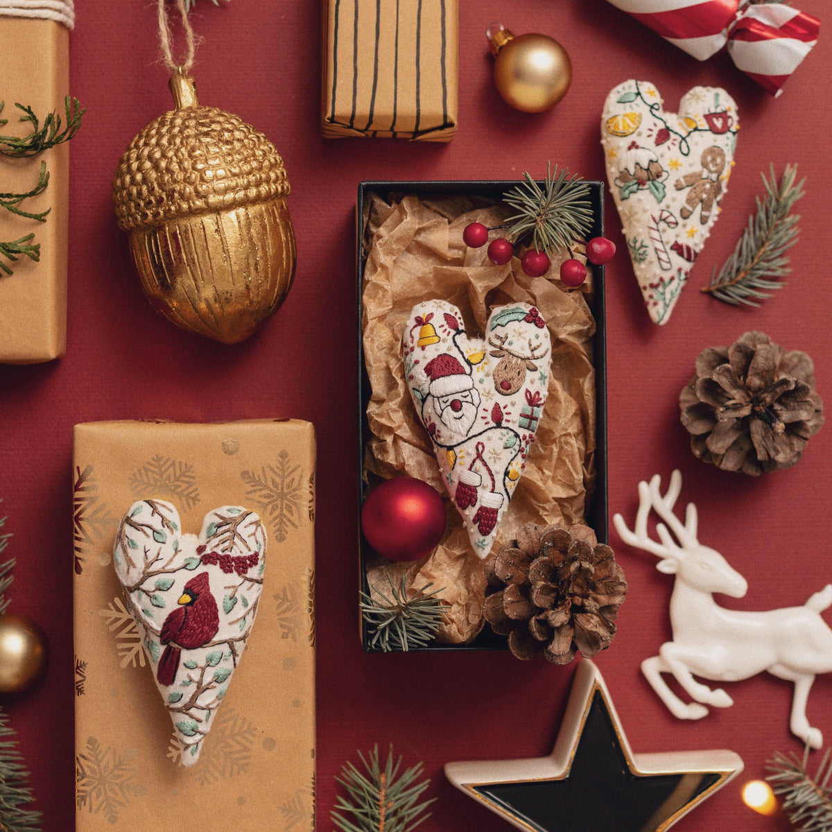 May include: A collection of handmade Christmas ornaments, including a heart-shaped ornament with a Santa Claus design, a heart-shaped ornament with a cardinal design, and a gold acorn ornament.
