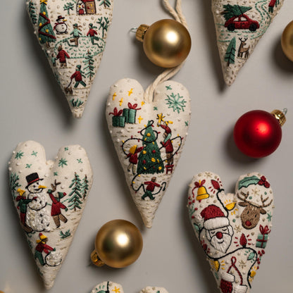 May include: A set of six handmade heart-shaped ornaments with embroidered Christmas scenes. The ornaments feature a snowman, a Christmas tree, Santa Claus, a reindeer, and other festive imagery. The ornaments are decorated with red, green, and white