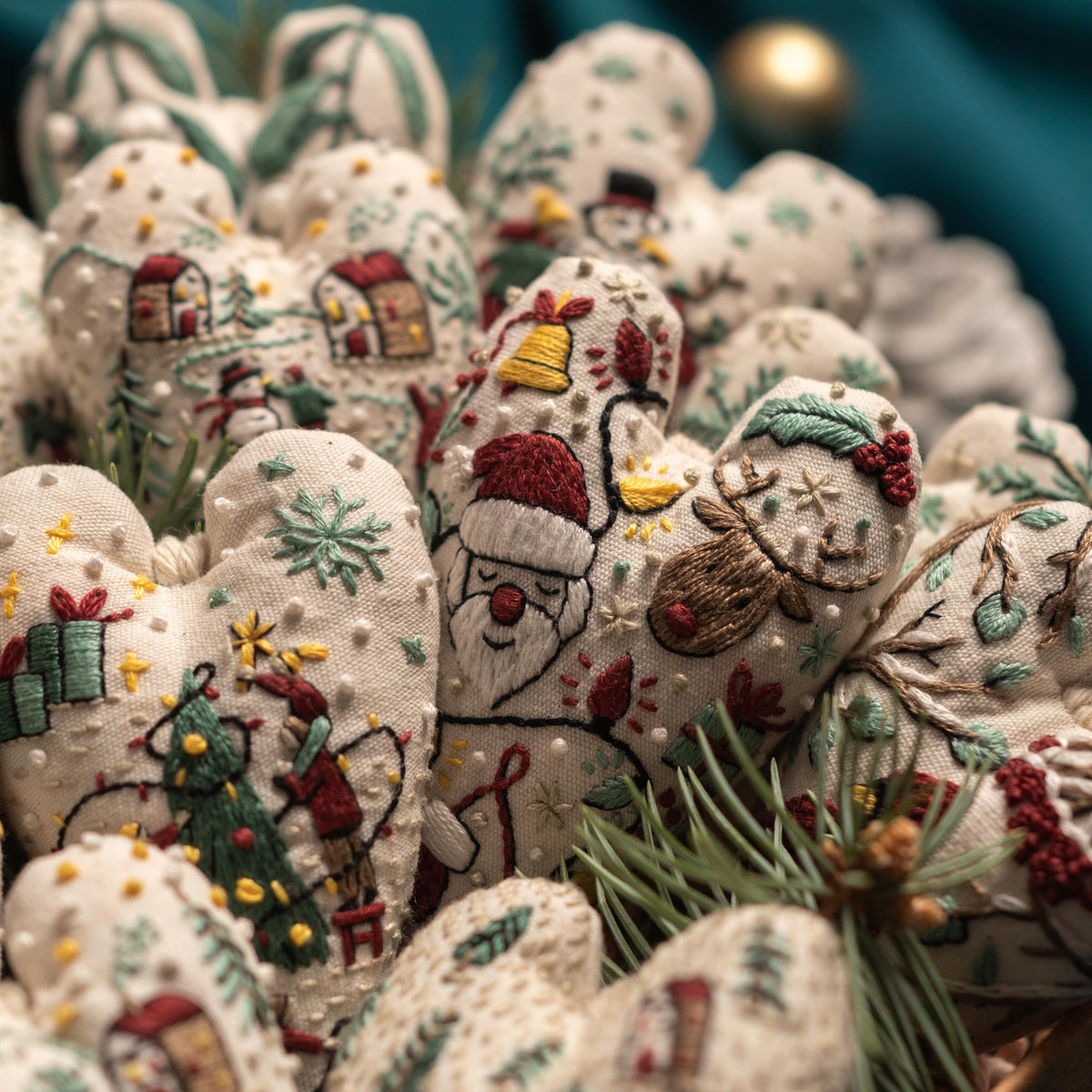 May include: A collection of handmade felt Christmas ornaments in the shape of hearts. Each heart features a different embroidered design, including a snowman, a reindeer, a Christmas tree, and Santa Claus. The ornaments are a soft white color with r